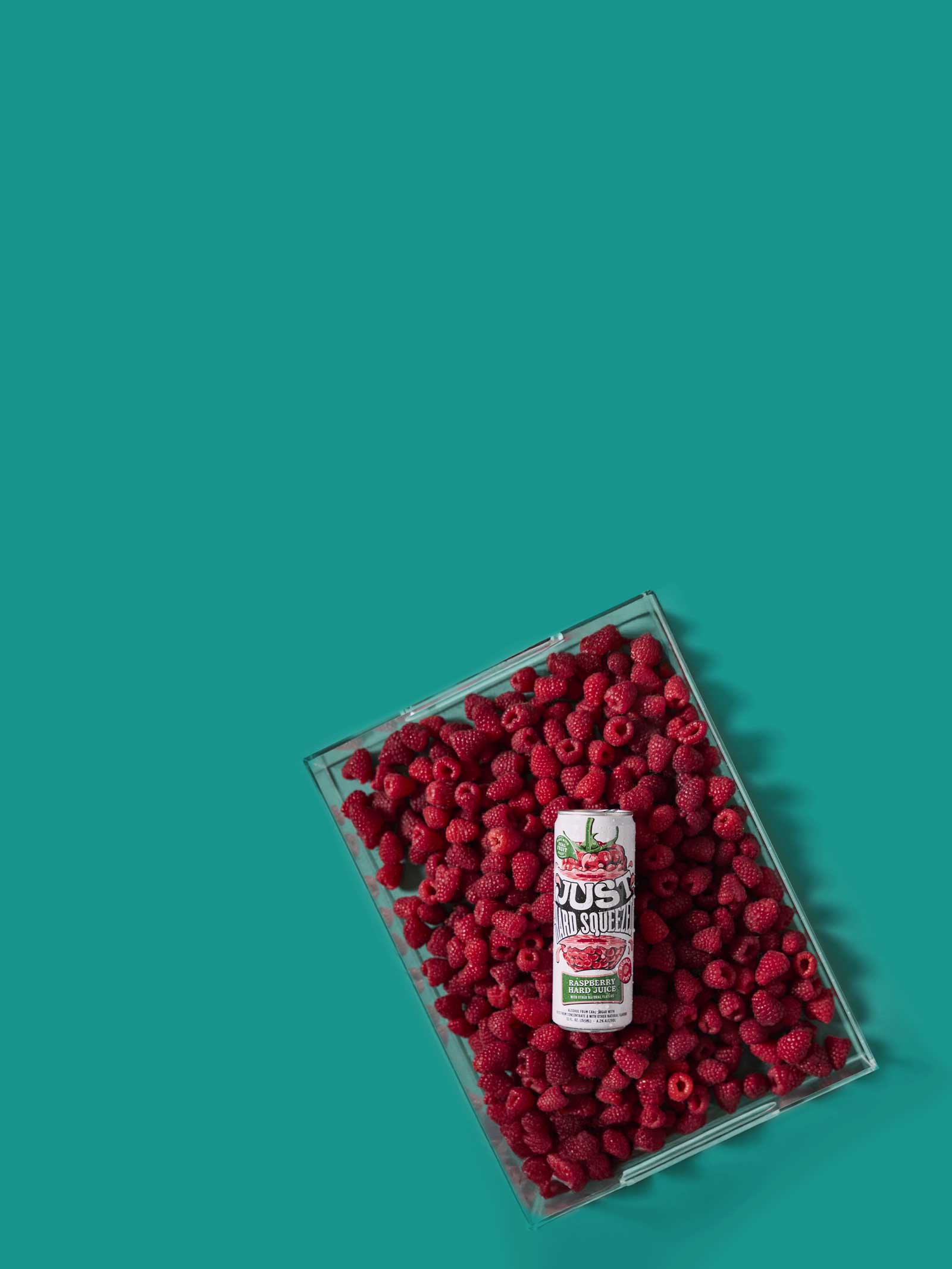 can of just hard squeezed raspberry laying on a bed of fresh raspberries