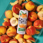 can of just hard squeezed peach laying on a bed of fresh peaches