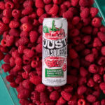 can of just hard squeezed raspberry laying on a bed of fresh raspberries