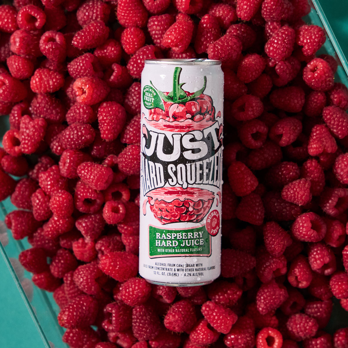 can of just hard squeezed raspberry laying on a bed of fresh raspberries