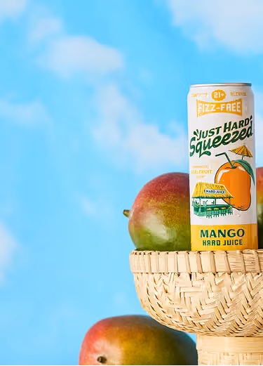 A basket with mangoes and Just Hard Squeezed Mango in front of clouds